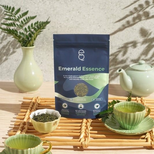 Tea packaging labeled 'Emerald Essence' with tea cups and a teapot on a wooden surface.