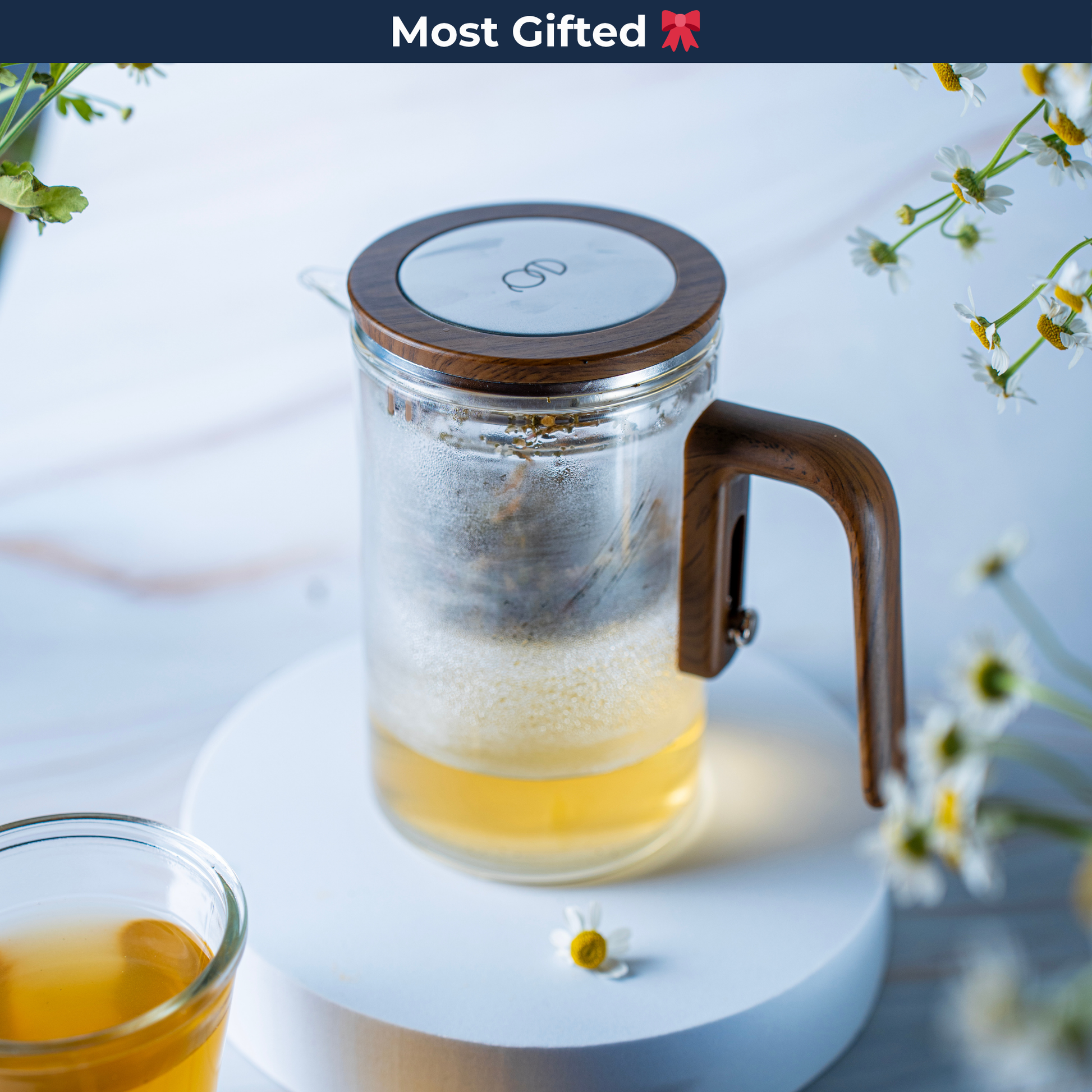 EQ Tea Steeper on a circular stand with flowers and a teacup in the background